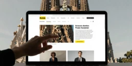Mano interactuando con una web de contenidos frente al paisaje urbano de Barcelona, una escena que simboliza cómo las top agencias de marketing de contenidos en Barcelona convierten historias, diseño y estrategia digital en experiencias que capturan la atención y construyen marca.